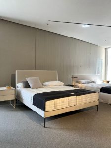 Showroom bedroom display with a white upholstered platform bed, two pillows, a gray throw pillow, and a black blanket at the foot of the bed.