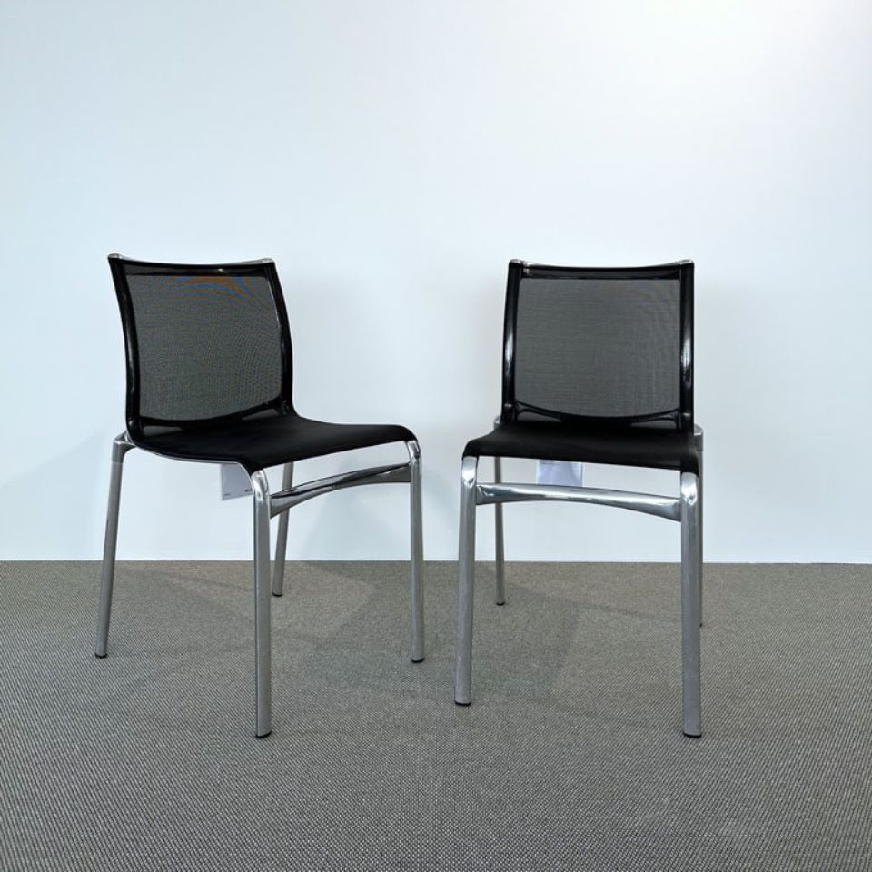 Two black mesh-back chairs with metal legs spaced apart in a minimal office setting.