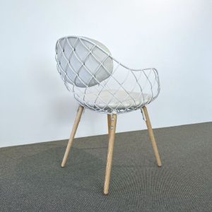 White wire lattice chair with light wood legs on a gray carpet and pale wall background.