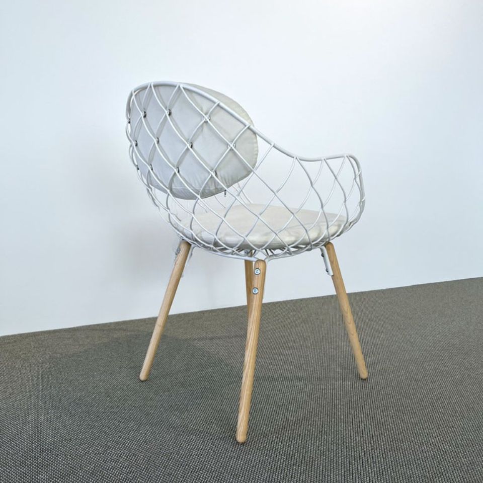White wire lattice chair with light wood legs on a gray carpet and pale wall background.