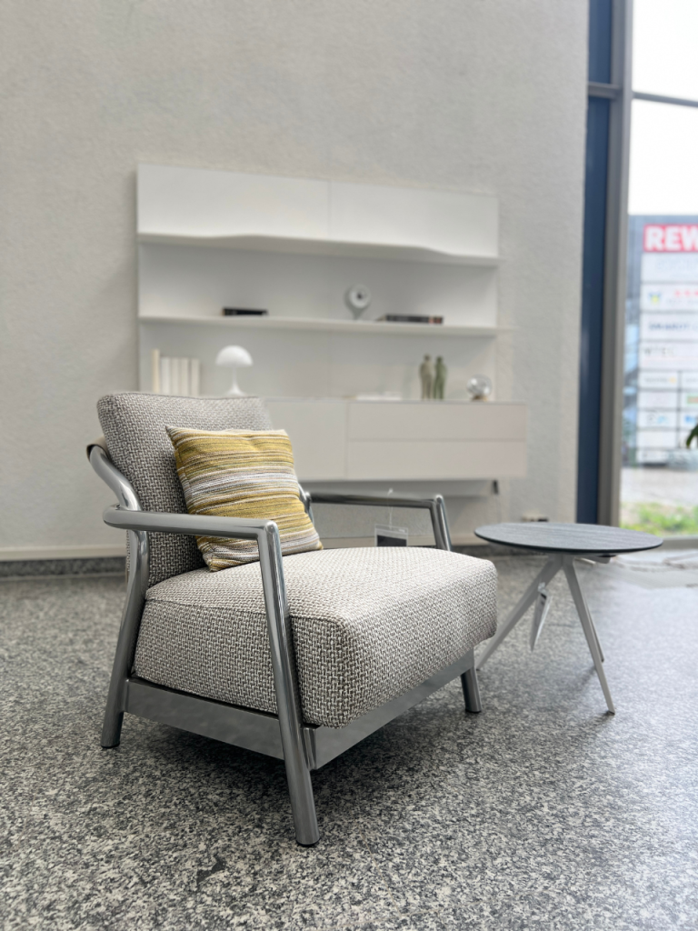 Modern grey fabric armchair with metal frame and a striped cushion, paired with a small round coffee table in a minimalist showroom.