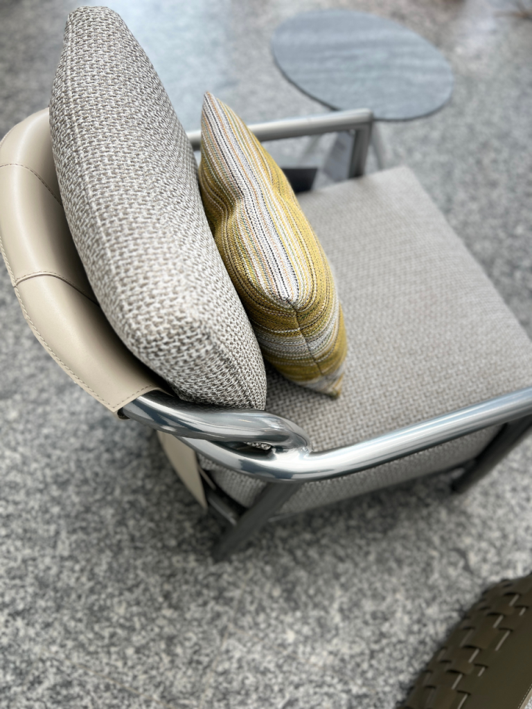 Outdoor chair on a stone patio with textured gray cushions and a yellow striped pillow.