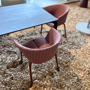 Outdoor seating area with pink, ribbed chairs around a dark metal table on a wood-chip ground surface.
