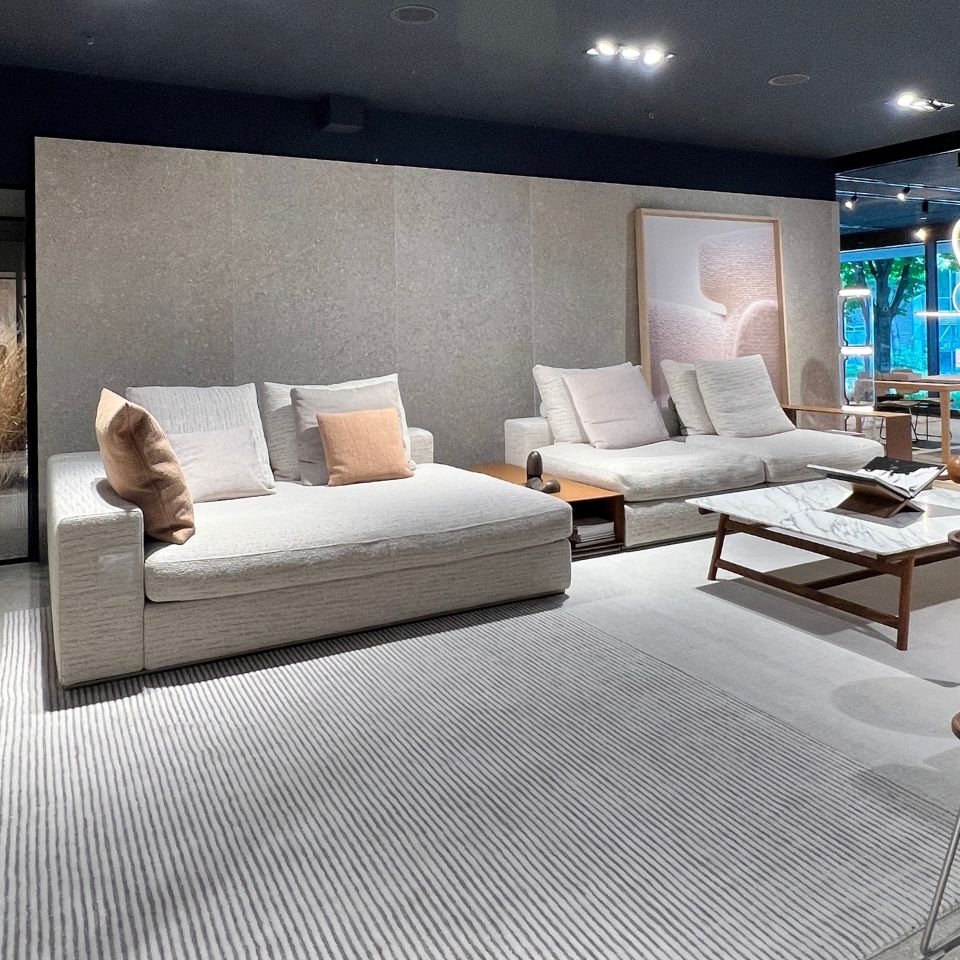 Modern showroom living room with two beige sofas, neutral pillows, and a marble coffee table.