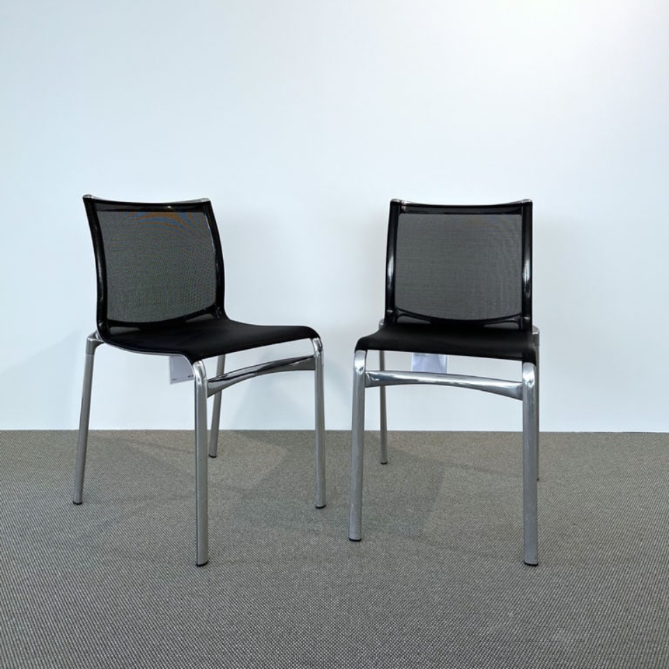 Two black mesh-back chairs with metal legs in an empty, light-filled room on a gray carpeted floor