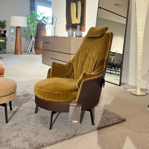 Velvet mustard-yellow lounge chair with a dark brown base and black legs in a modern showroom on a beige rug.
