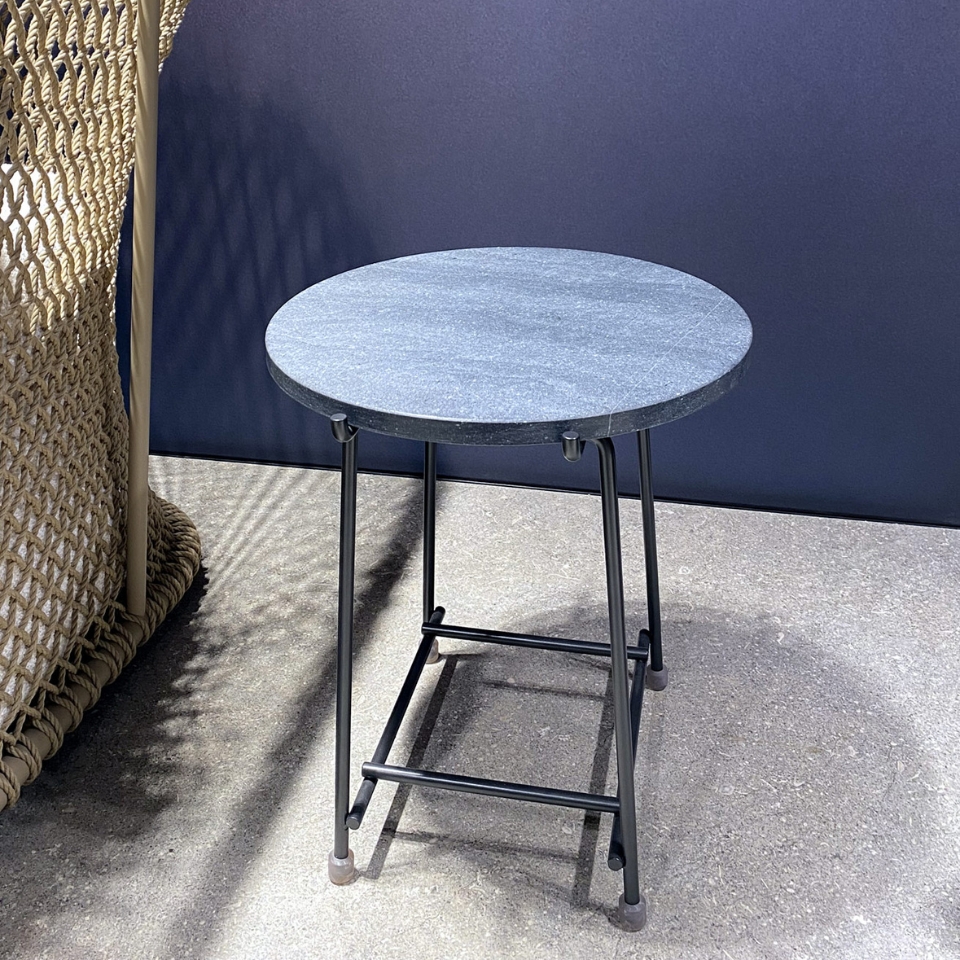 Round metal patio table with a speckled grey top on a sunlit concrete surface beside a woven outdoor chair.
