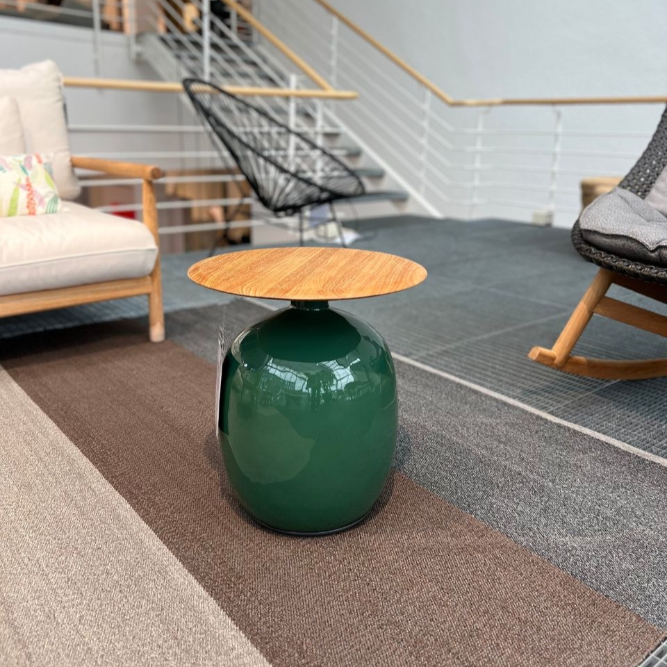 Green glossy ceramic stool with a round natural wood top, shown in a contemporary living-room showroom setting.