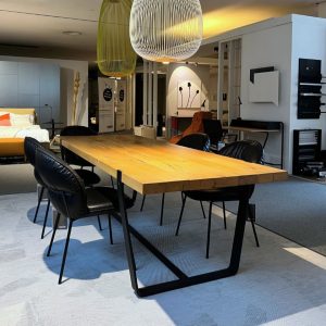 Modern furniture showroom with a large wooden dining table and black leather chairs under oversized pendant lights.