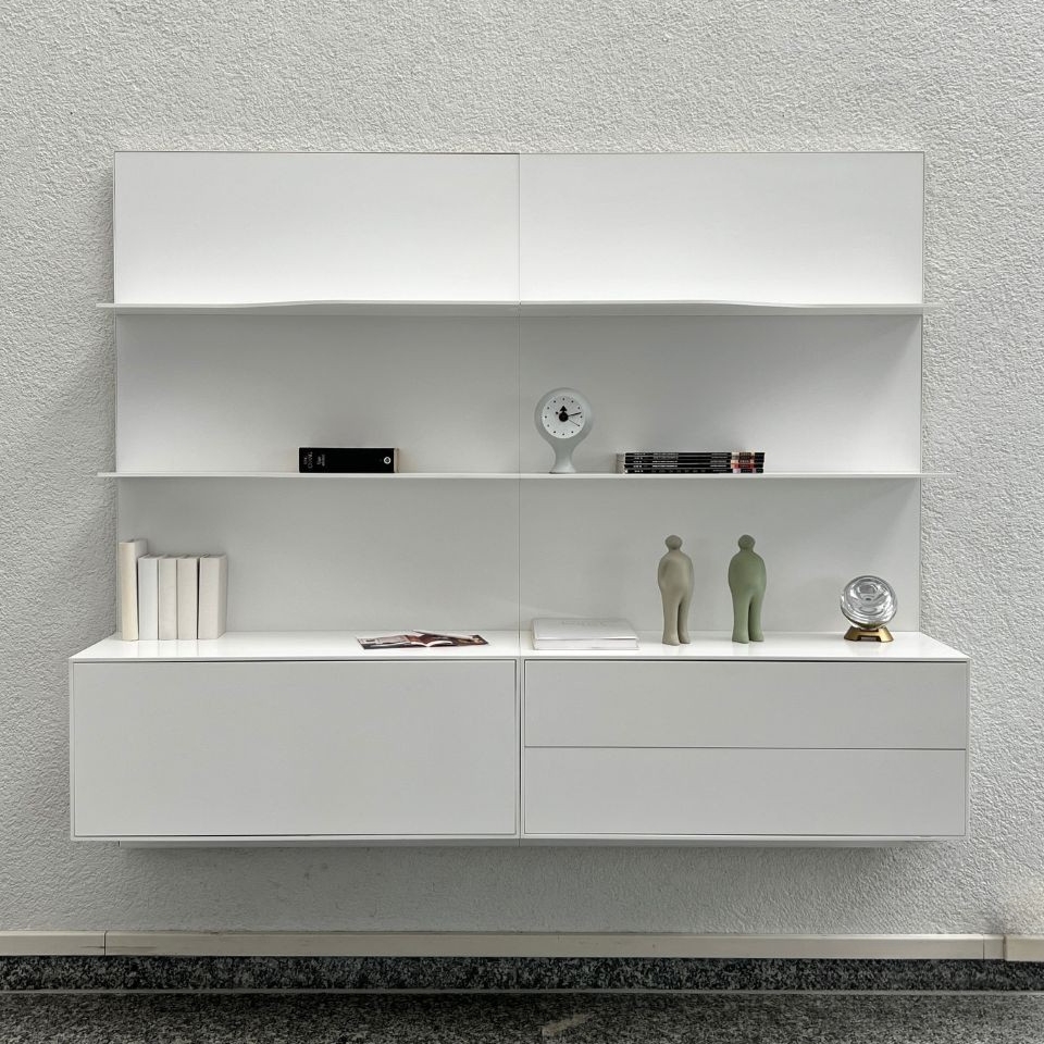 White modern wall-mounted shelving unit with closed cabinets and open shelves, minimal decor on display.