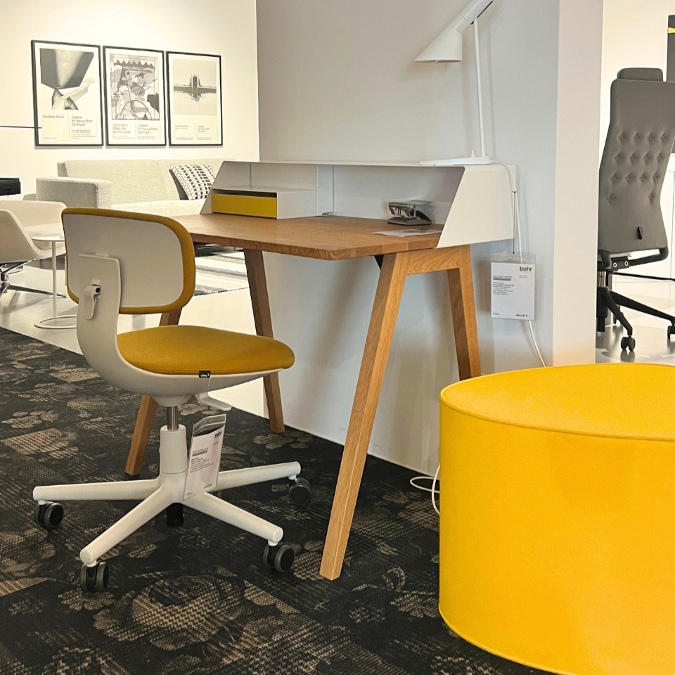 Mid-century wooden desk with white storage and mustard-yellow swivel chair, plus a bright yellow round ottoman in a showroom setting.