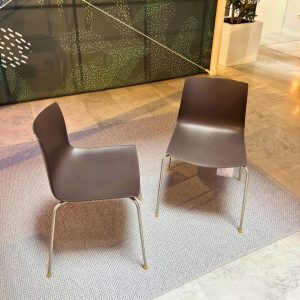 Two gray plastic chairs with metal legs sit on a light rug in a modern indoor space, facing slightly toward each other.