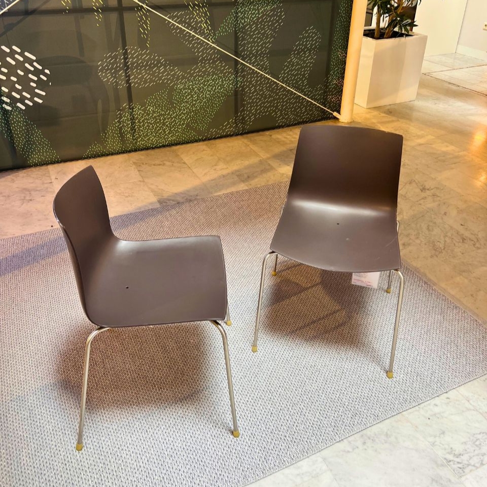 Two gray plastic chairs with metal legs sit on a light rug in a modern indoor space, facing slightly toward each other.