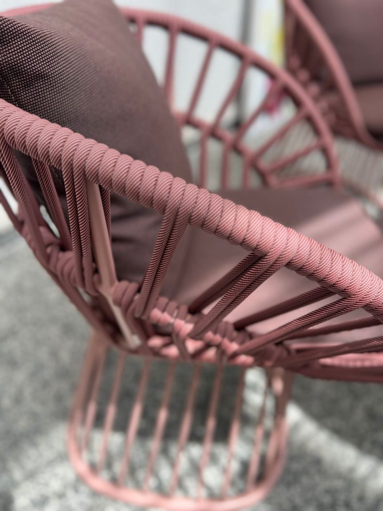 Close-up of a pink rope-woven outdoor chair, showing braided strands and curved frame.