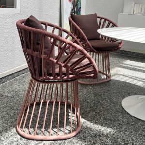 Two pink wicker-style patio chairs with brown cushions around a white round table on a speckled outdoor patio.
