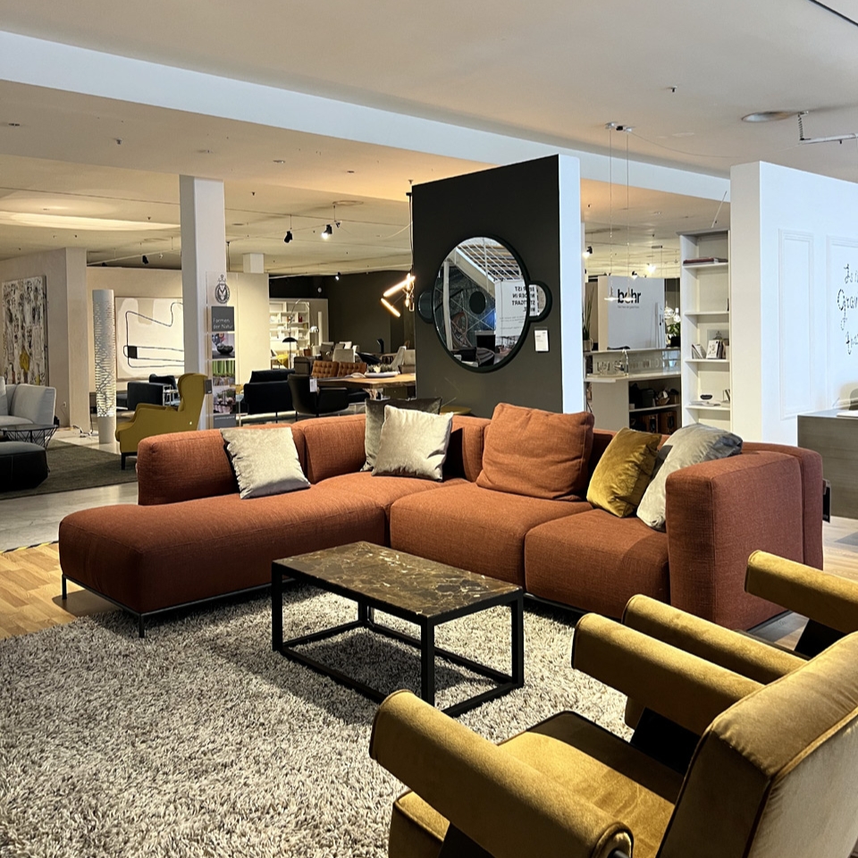 A modern showroom living room with an orange sectional sofa, a marble-top coffee table, and mustard-yellow chairs on a gray rug.
