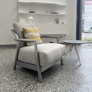 Modern gray upholstered armchair with metal frame and striped cushion, beside a small round table in a showroom setting.