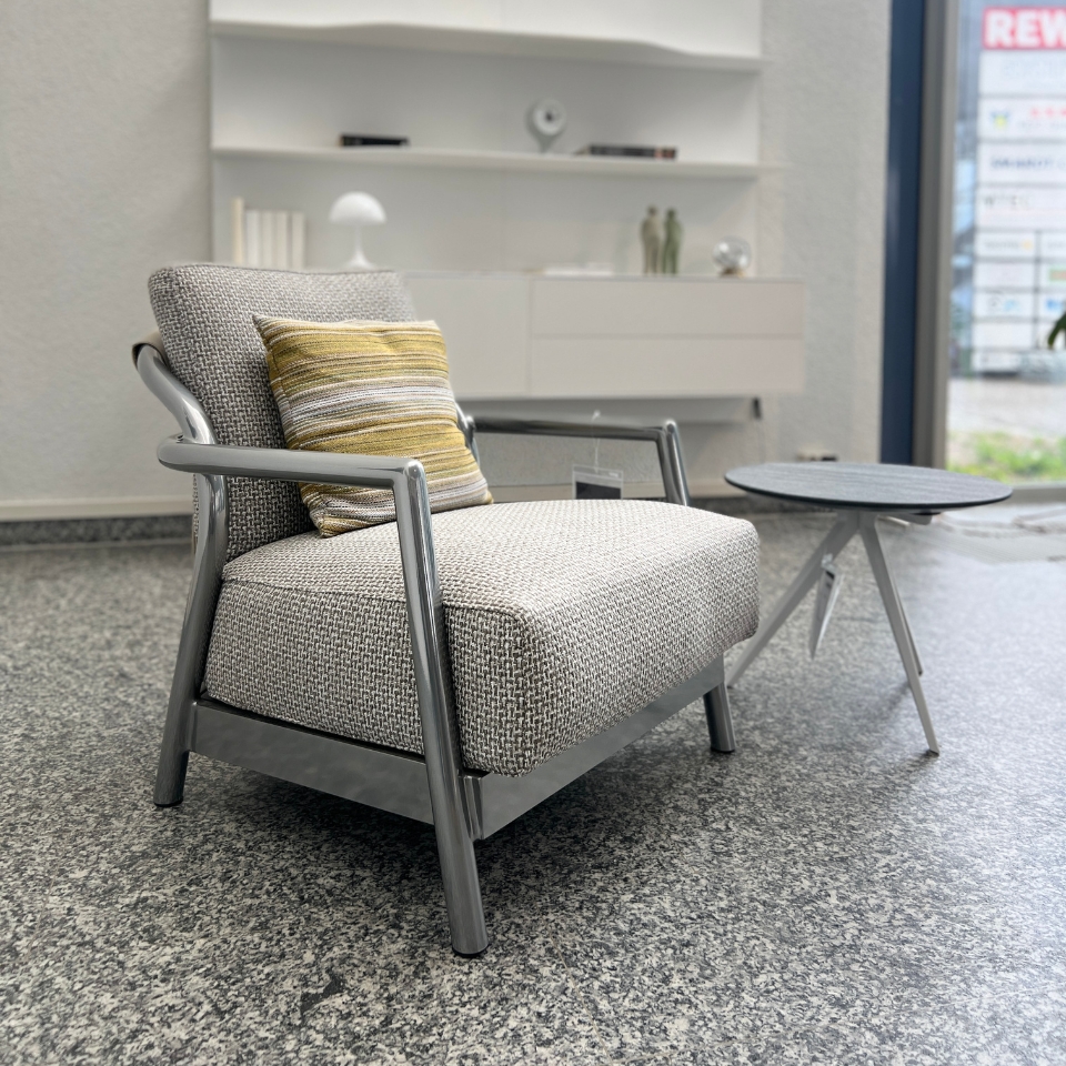Modern gray upholstered armchair with metal frame and striped cushion, beside a small round table in a showroom setting.