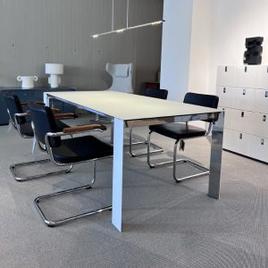 Modern conference room with a white rectangular table and black cantilever chairs, chrome frames, and grey walls with storage lockers nearby.