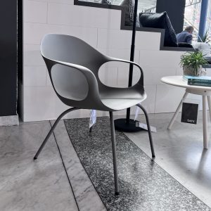 Modern gray molded chair with curved armrests on metal legs, in a showroom beside a round white table and books.