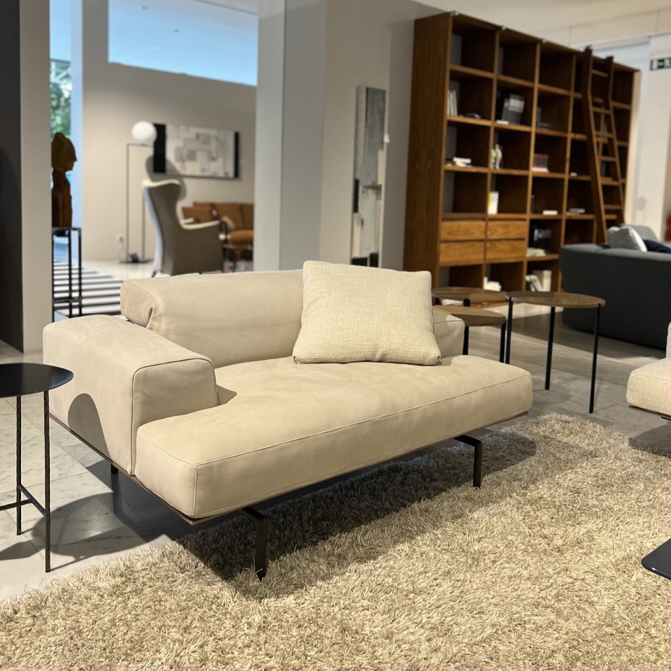 Beige sofa with a single cushion on a shag rug in a modern furniture showroom.