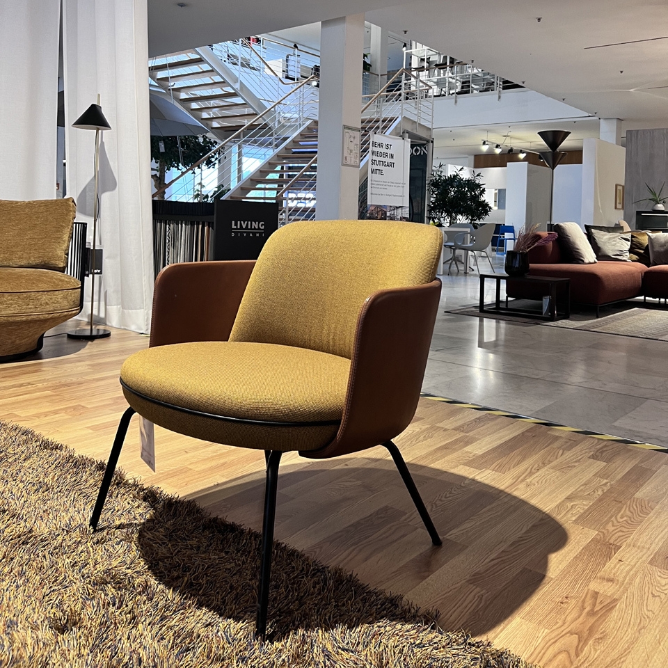 Mustard-yellow upholstered chair with brown armrests and black legs in a modern furniture showroom.