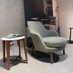 Green boucle armchair with wooden legs beside a round white side table in a modern showroom.