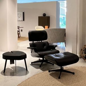 Black leather lounge chair with matching ottoman, a small round black table, and a woven rug in a modern showroom.