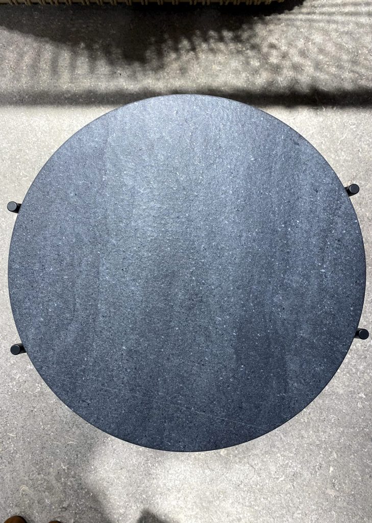 Top-down view of a round, dark granite table on a concrete surface with small edge knobs visible.