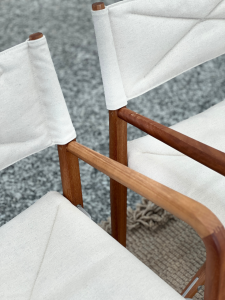 Close-up of two light beige fabric cushions on a wooden outdoor chair frame, showing fabric-wrapped backrests and curved armrests.