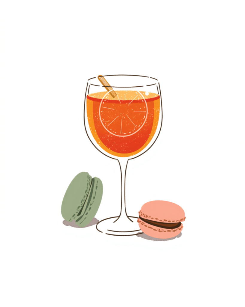 Glass of orange cocktail with a citrus slice and straw, flanked by green and pink macarons.