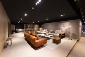 Modern showroom lounge with an orange sofa set and gray sectionals arranged around a white coffee table.",