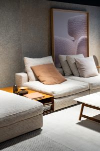 Beige sectional sofa with neutral pillows in a modern living room; a large framed image leans against a textured gray wall.