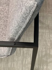 Close-up of grey fabric upholstery on a chair seat and its black metal frame at the corner.