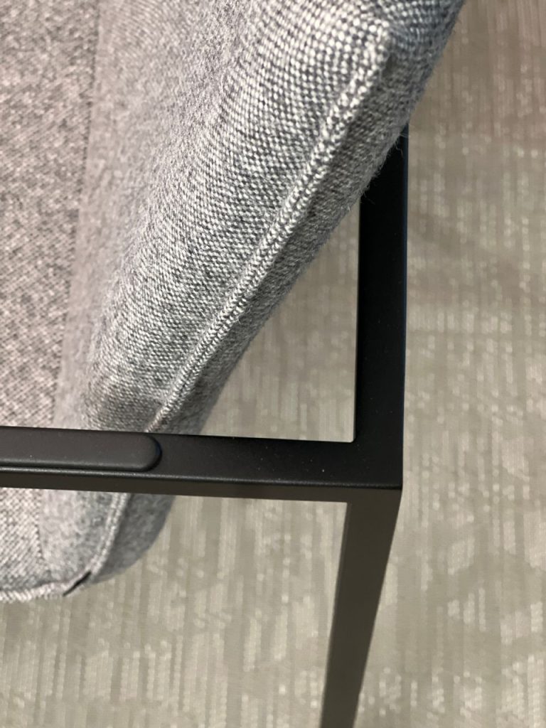 Close-up of grey fabric upholstery on a chair seat and its black metal frame at the corner.