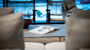 Open magazine on a marble coffee table in a cozy living room with soft beige seating and a blurred blue-toned background.