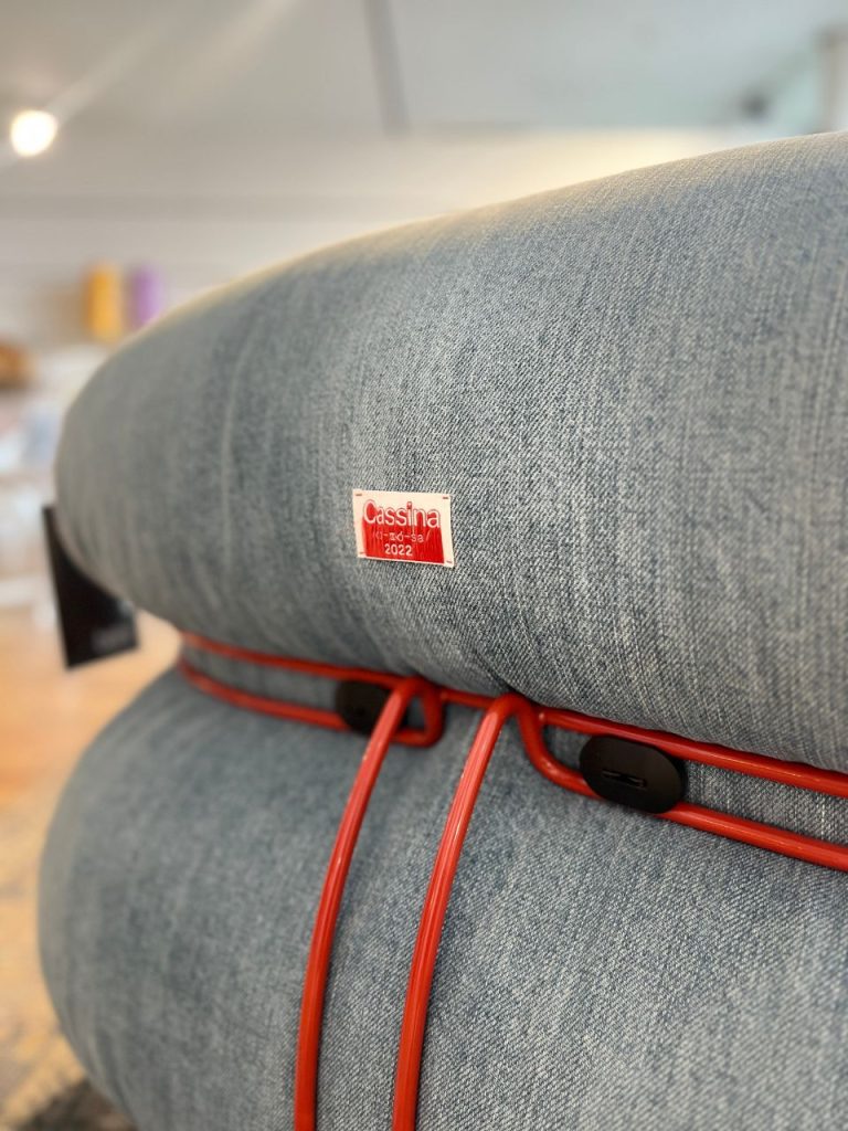 Close-up of blue denim upholstery on a chair with a red cord and a small Cassina tag reading 2022.