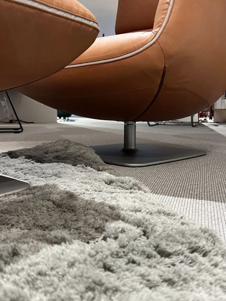 Close-up of a brown leather swivel chair on a metal pedestal in an office, with a gray shag rug in the foreground.