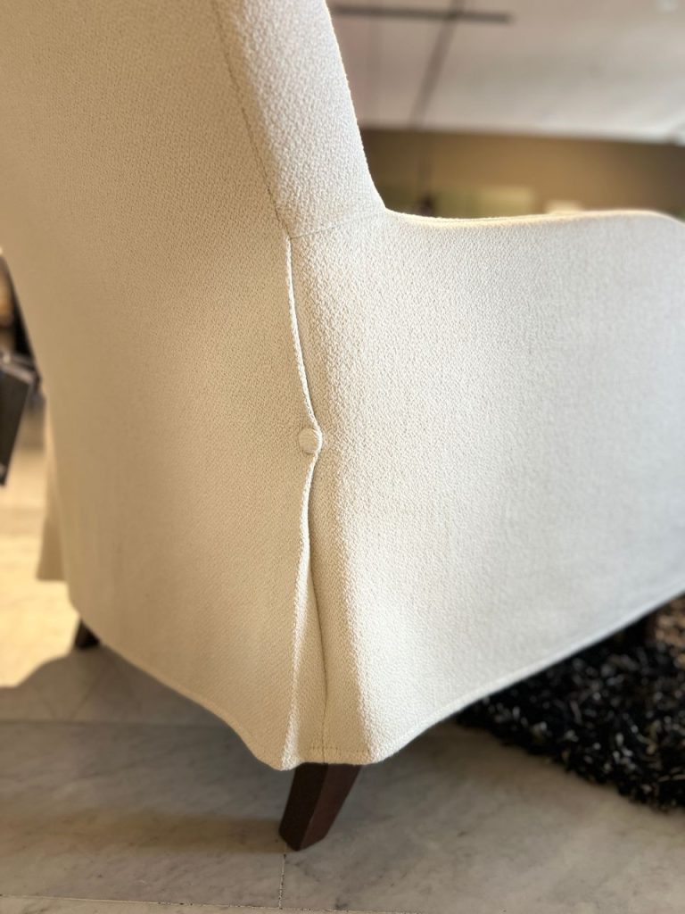 Close-up of a light beige upholstered chair showing a vertical seam and a wooden leg on a tiled floor.