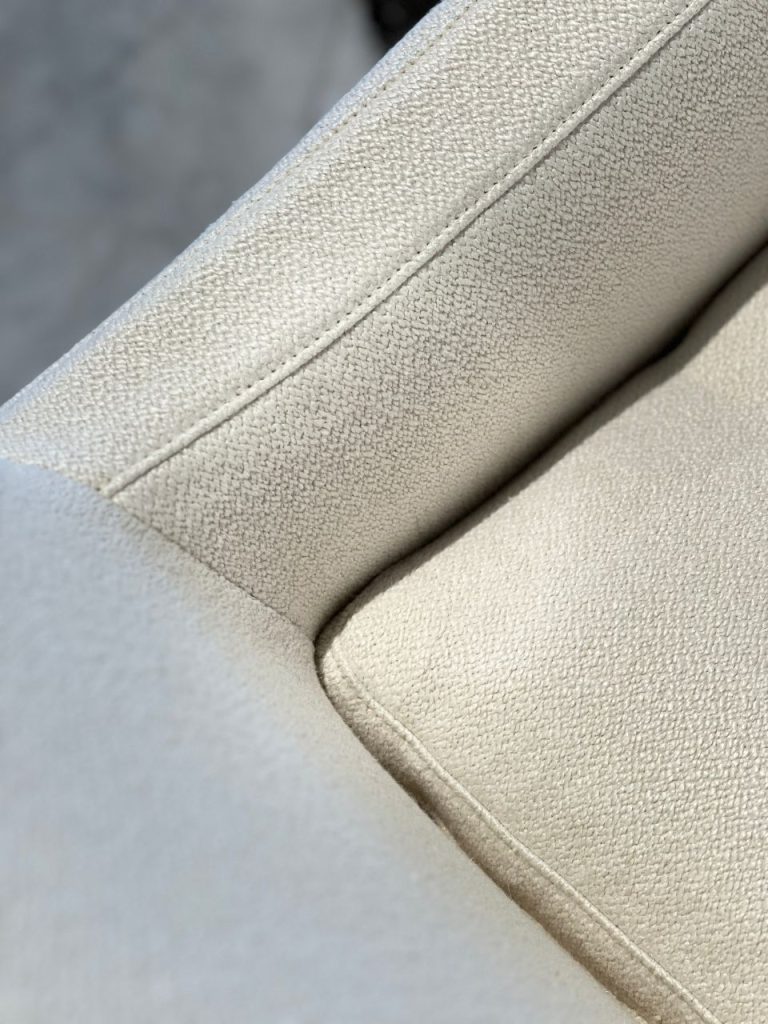 Close-up of beige textured car seat upholstery with a stitched seam.”