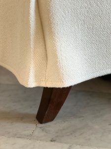 Close-up of a dark wooden sofa leg supporting a beige textured upholstered couch on a marble floor.