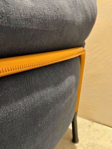 Close-up of an orange chair frame resting along a dark blue upholstered chair, showing the seam and textured fabric.