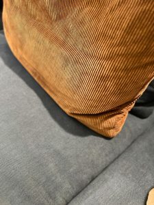 Close-up of a brown corduroy cushion with ribbed texture resting on a gray sofa.