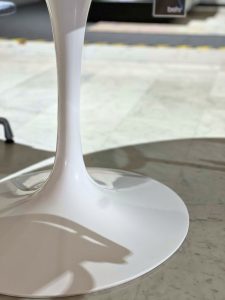 Close-up of a white, glossy wine glass stem and round base resting on a marble surface, with a blurred background.