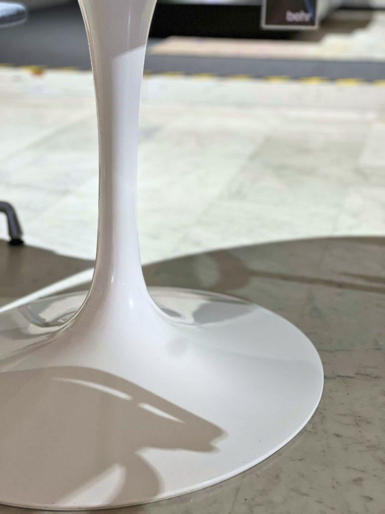 Close-up of a white, glossy wine glass stem and round base resting on a marble surface, with a blurred background.