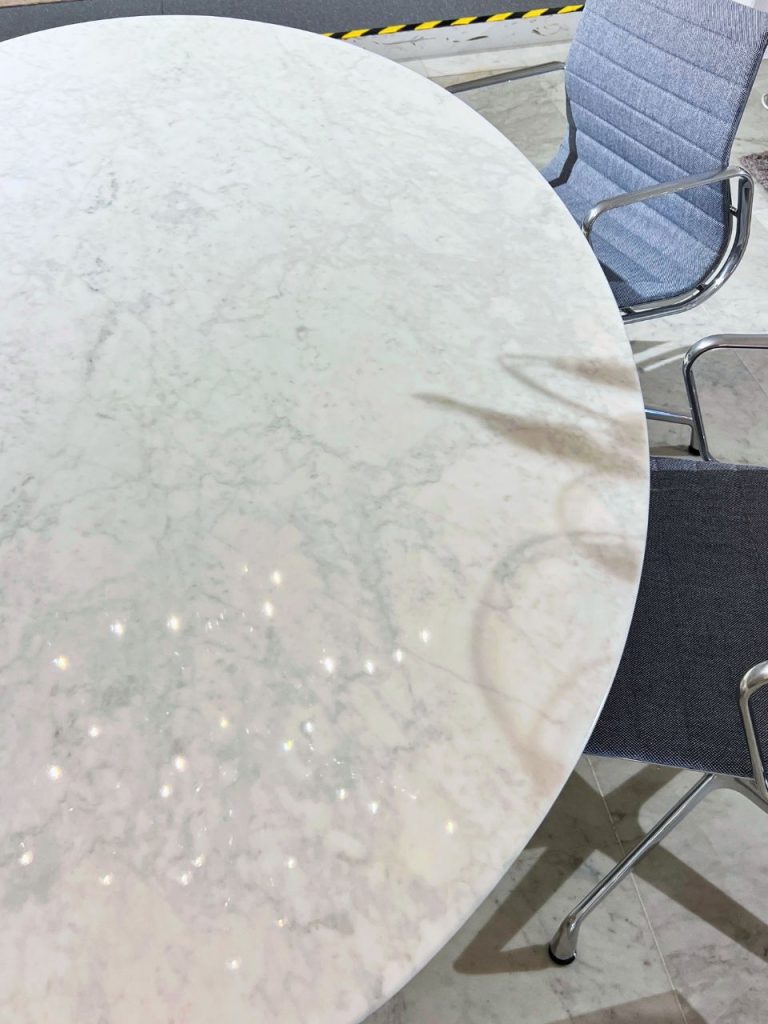 Round white marble table with gray veining and metal-legged chairs visible at the edge of the frame.