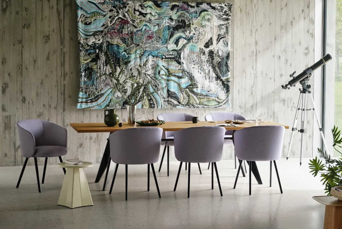 Modern dining room with a wooden table and lavender chairs, large abstract wall hanging, and a telescope on a tripod by the window.
