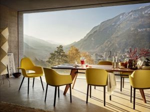 Modern dining area with yellow chairs around a long table, overlooking mountains and a distant city.