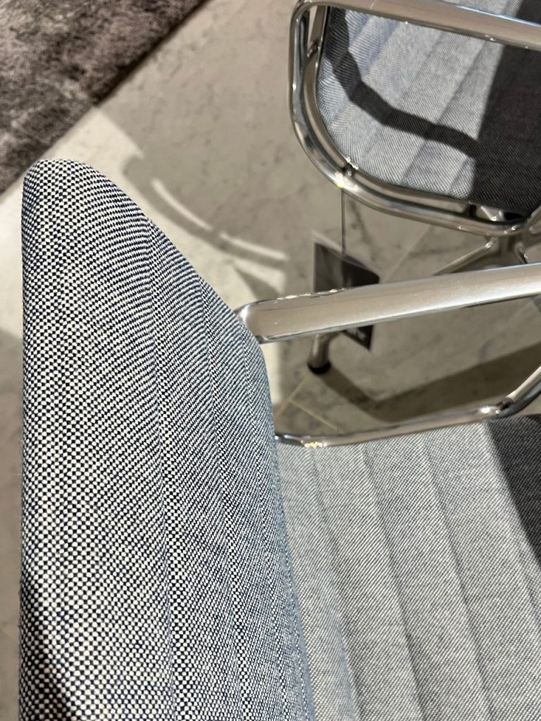 Close-up of a modern office chair with blue-gray fabric and chrome frame, showing the seat and arm support.