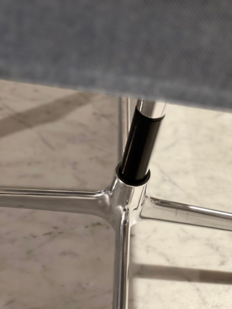 Close-up of a chrome chair leg junction with a black adjustable support tube threaded into the leg.